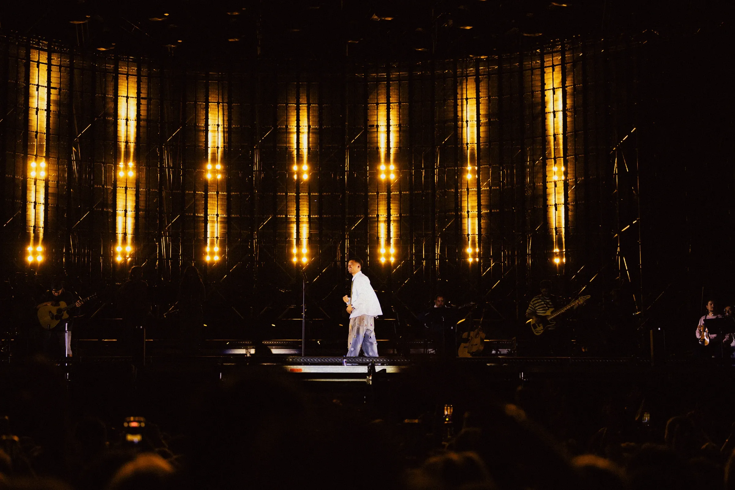 Singer in white beneath vertical golden stage lights