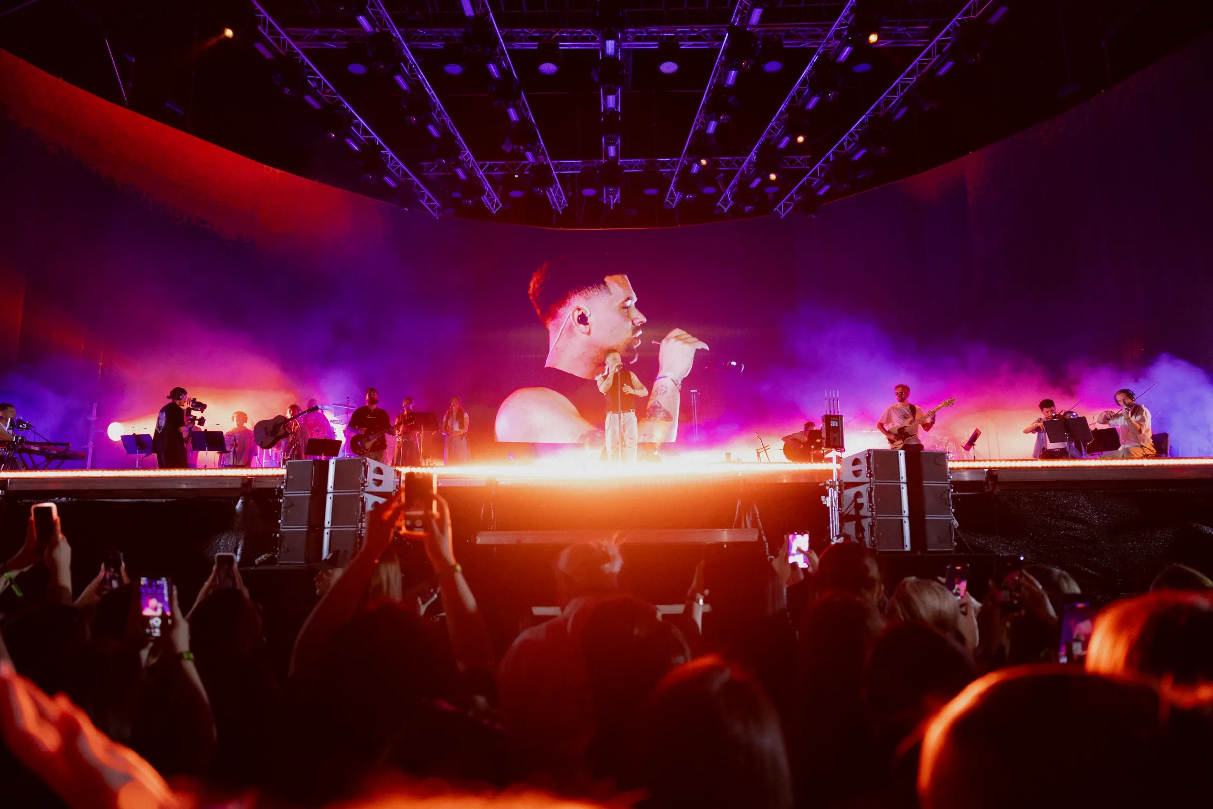 View from the audience of the singer and band under purple lighting
