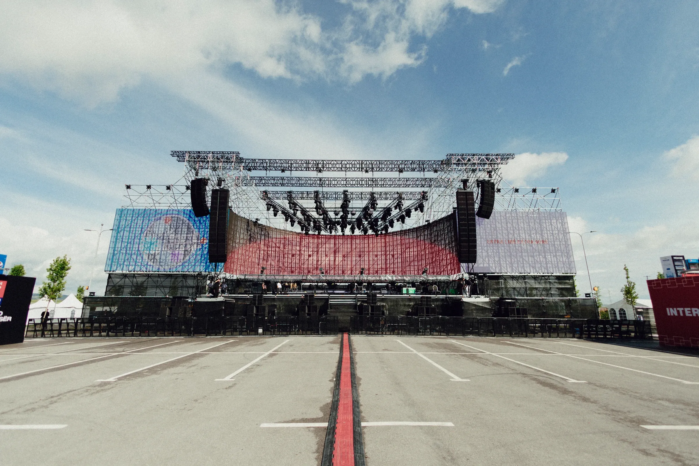 Outdoor stage with a curved LED screen and overhead lighting rig, viewed from the audience area