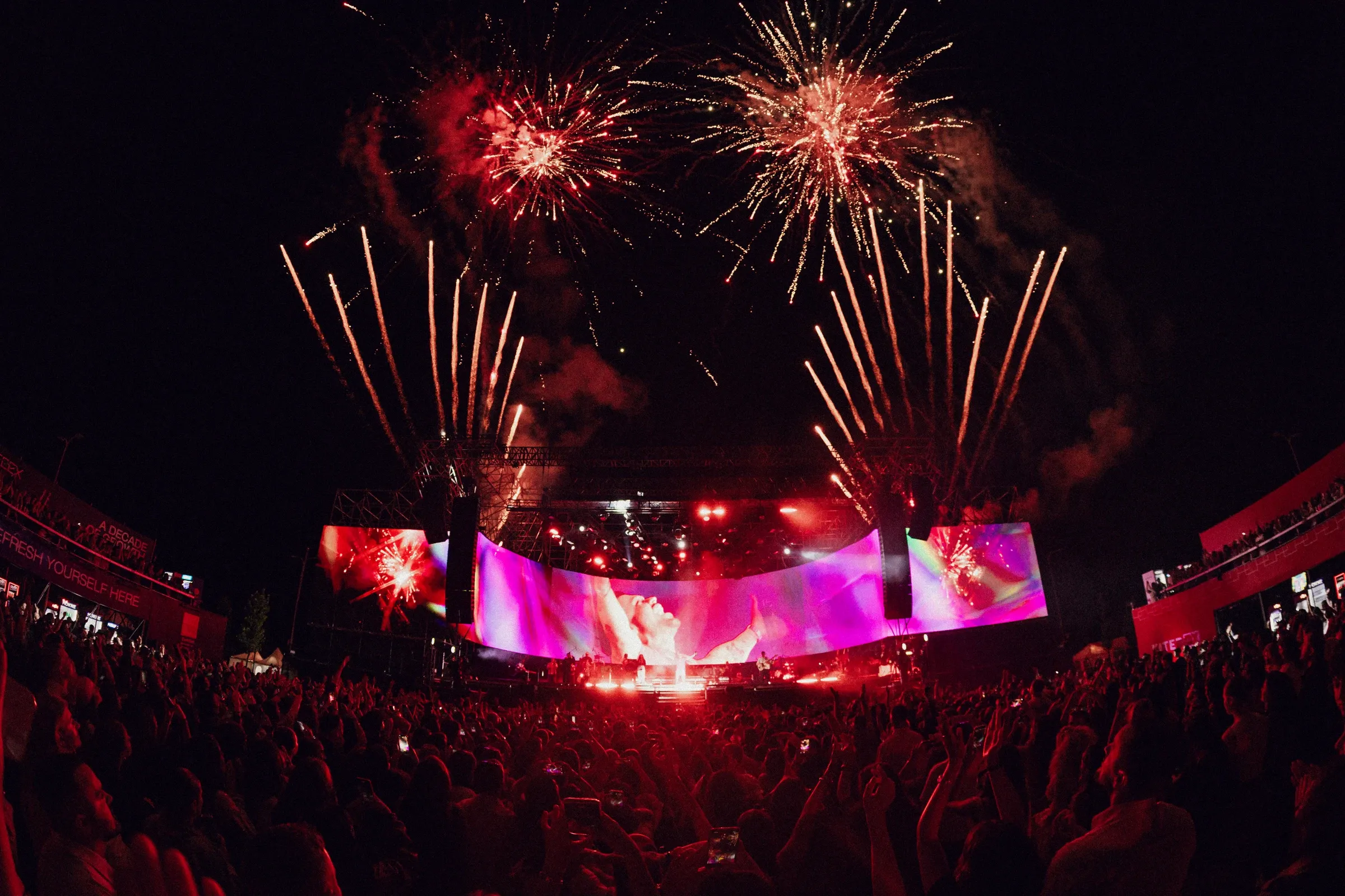 Fireworks above the illuminated outdoor stage and concert audience at night